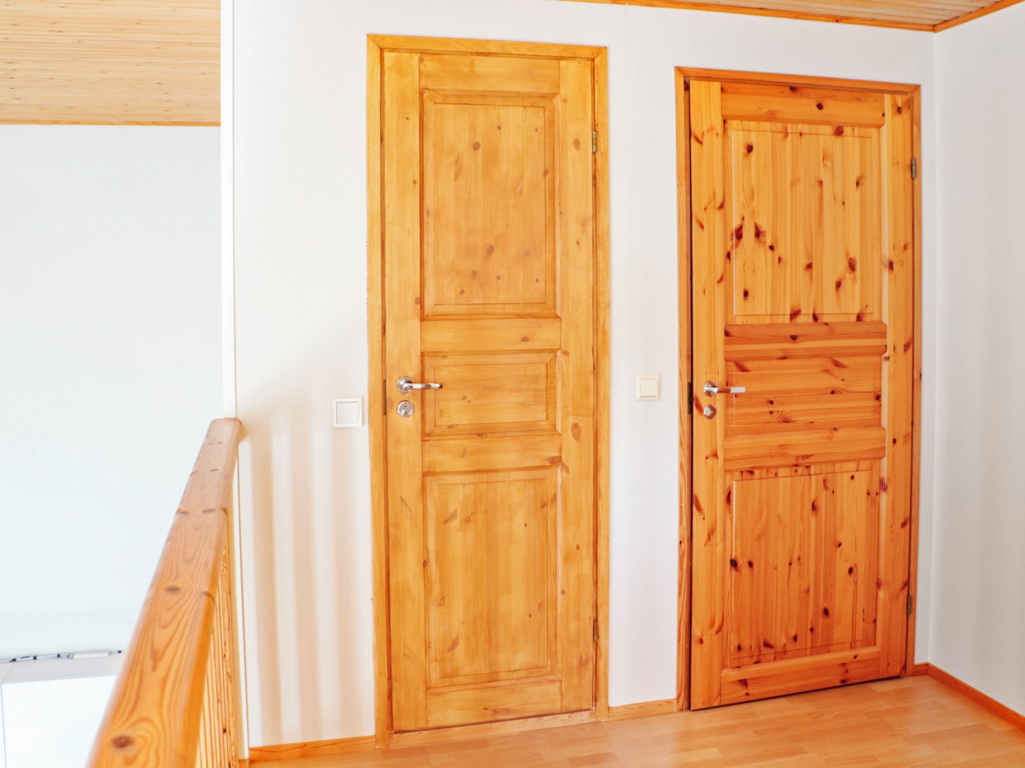 Deux portes en bois dans une pièce aux murs blancs et au plancher en bois.