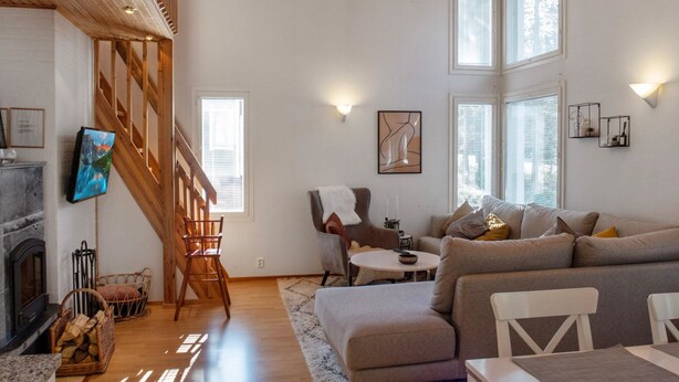 A spacious living room with a fireplace, wooden staircase, and large windows.