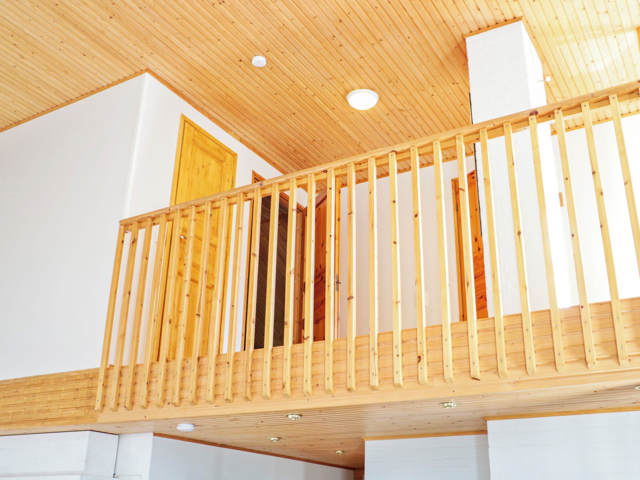 Un balcón de madera con barandilla, paredes blancas y techo de madera.