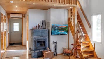 A spacious living room with a stone fireplace, a television mounted on the wall, and a wooden staircase.