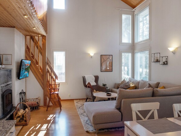 Amplia sala de estar con chimenea, techo alto con vigas de madera, un ventanal grande y un rincón de descanso acogedor.