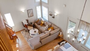 A spacious living area with a sofa, coffee table, and dining table. There are multiple windows providing natural light.