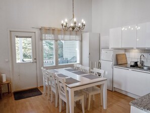 Espaço de refeições com mesa, cadeiras, geladeira e janela com persianas.
