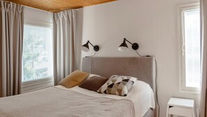 A bedroom with a bed, two wall-mounted lamps, a bedside table, and a window with curtains.