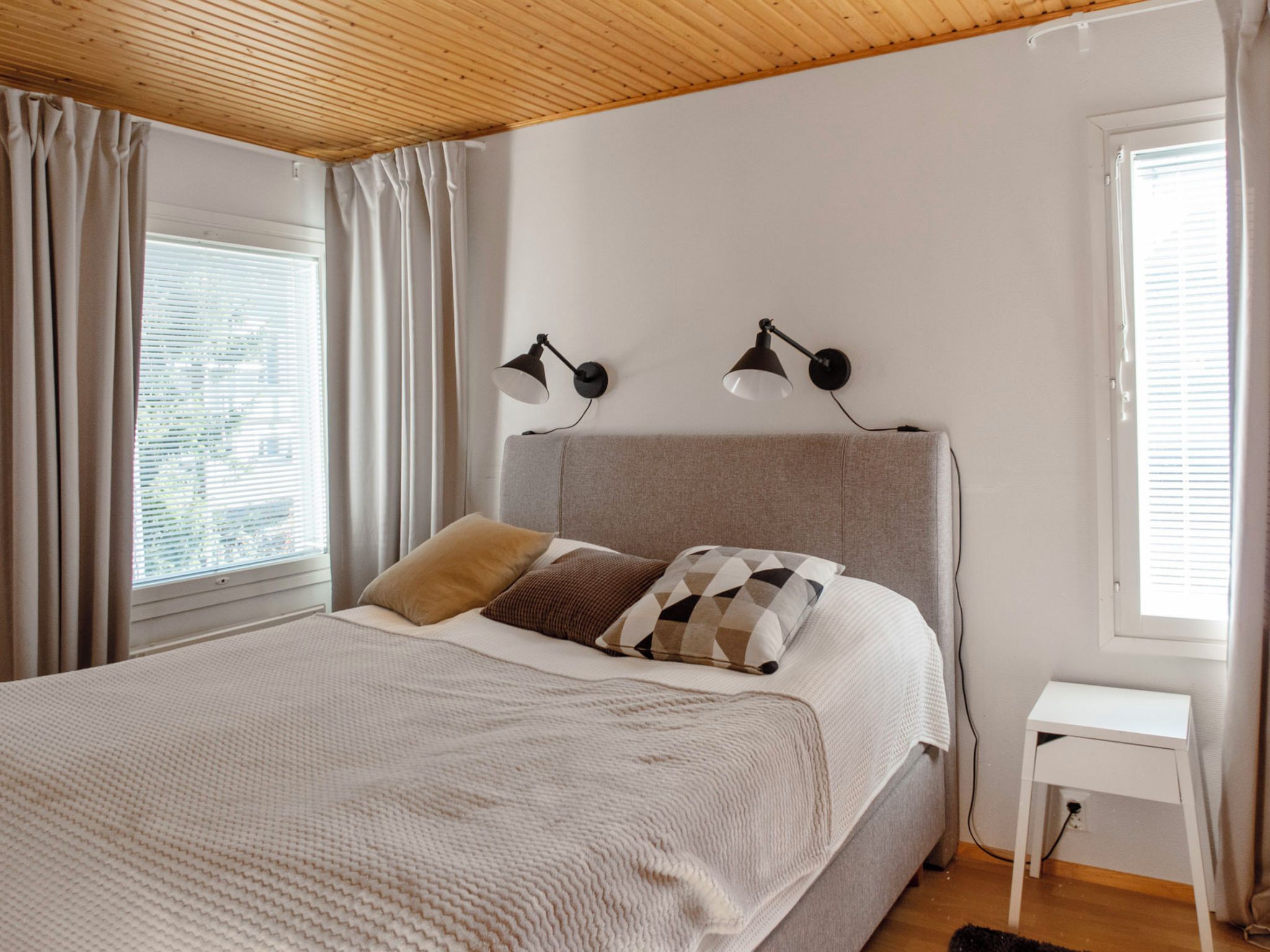 A bedroom with a bed, two bedside lamps, a nightstand, and a window with curtains.