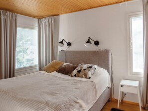 Un dormitorio con cama, dos lámparas de noche, una mesita de noche y una ventana con cortinas.