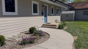 A single-story house with a blue door, a small front porch, and a landscaped garden with gravel and plants.
