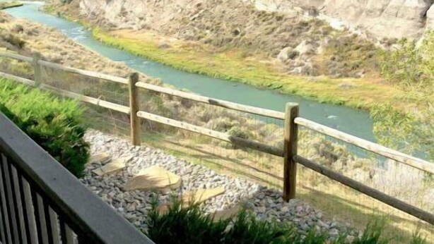 Vista d'una vall fluvial amb una tanca de fusta i un primer pla rocos.