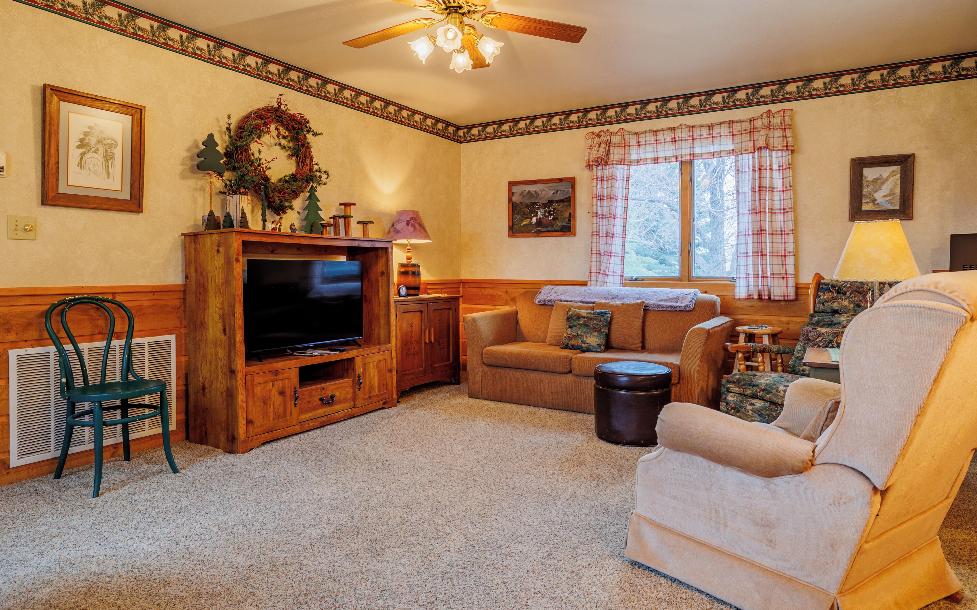 A cozy living room with a wooden entertainment center, a sofa, a chair, and a window with plaid curtains.
