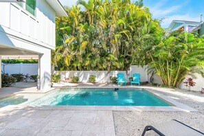 A swimming pool with a clear blue water, surrounded by a white wall and palm trees.