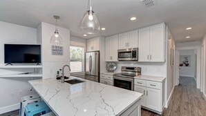 Una cocina moderna con armarios blancos, una isla de mármol, electrodomésticos de acero inoxidable e iluminación colgante.