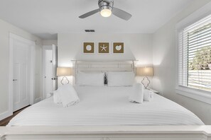 A neatly made bed with white linens, a ceiling fan, and wall-mounted lamps.