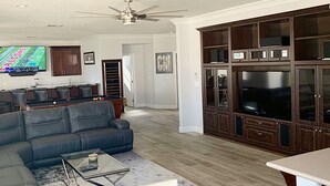 A living room with a sectional sofa, a glass coffee table, a pool table, and a large entertainment center with a flat-screen TV. - Five Bedroom Five Bath Residence  in Vegas  (Las Vegas)
