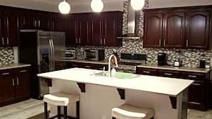 A modern kitchen with dark wood cabinets, stainless steel appliances, and a central island with bar stools. - Five Bedroom Five Bath Residence  in Vegas  (Las Vegas)