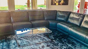 A sectional sofa, a glass coffee table, and a dark carpet in a living room. - Five Bedroom Five Bath Residence  in Vegas  (Las Vegas)