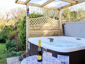 Un bain à remous, une bouteille de prosecco et un verre, le tout entouré d’une pergola en bois et d’un jardin.