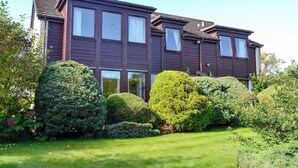A two-story house with a dark brown exterior, large windows, and a well-maintained garden with various shrubs and a lawn.