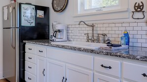 Una cocina con refrigerador, cafetera, lavamanos y un reloj en la pared.