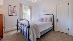 Un dormitorio con estructura de cama metálica, una puerta blanca y una ventana con cortinas.