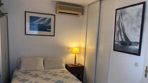 A hotel room with a bed, a nightstand with a lamp, an air conditioner, and two framed pictures on the wall. - Bleu Horizon Résidence by weekome (Les Abymes)