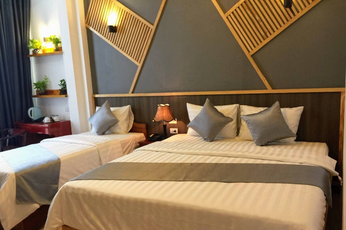 Habitació d'hotel amb dos llits, una taula, una làmpada i una estant amb plantes penjades a la paret.