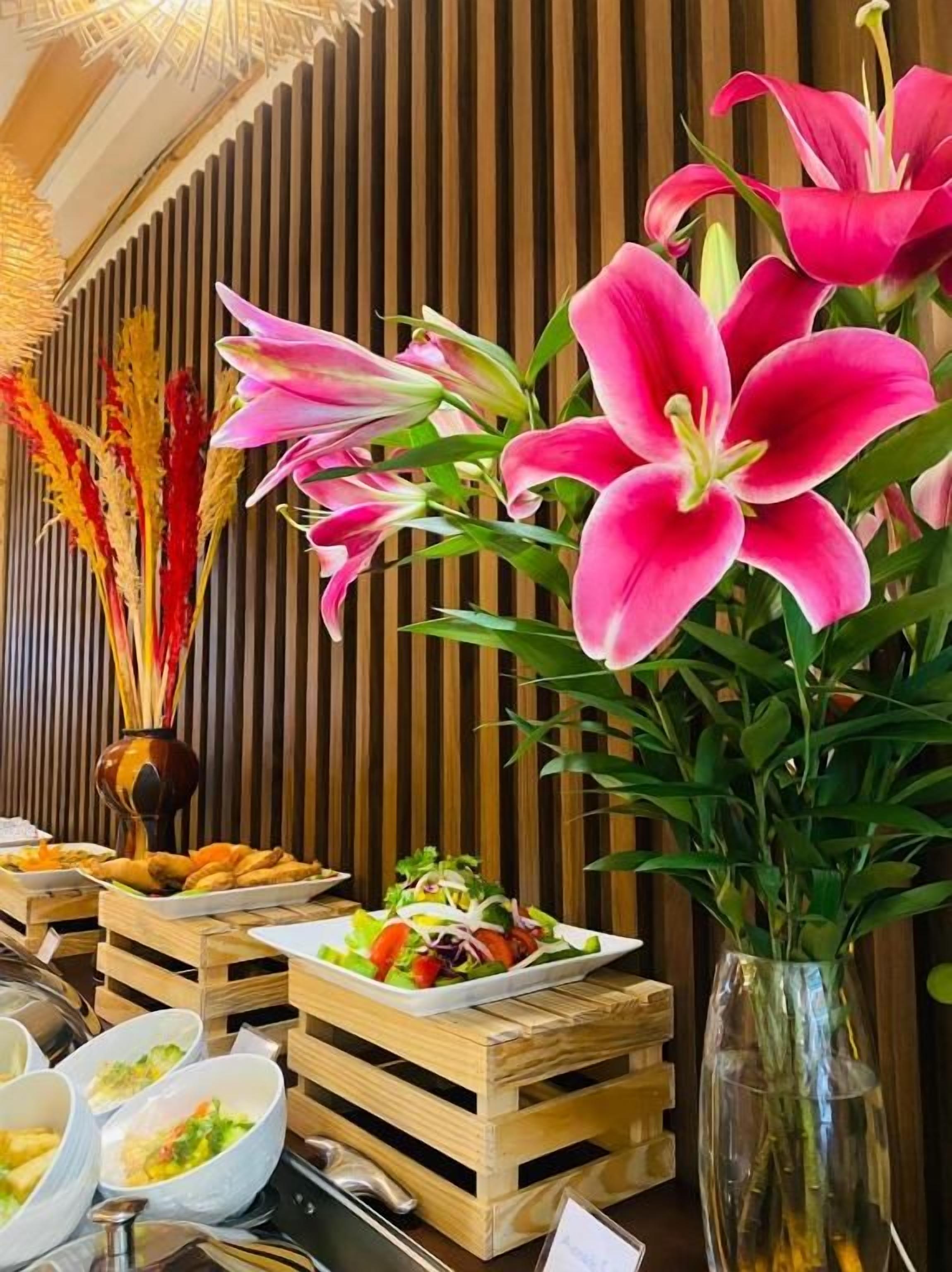 Un buffet proposant divers plats, agrémenté d’un vase rempli de lys roses.