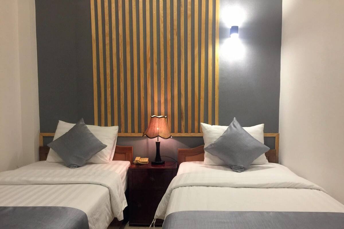 Habitació d'hotel amb dos llits, cadascun amb un almoïna i una taula de nit amb una làmpada.