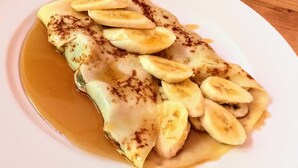 Ein Teller mit Pfannkuchen, Bananenscheiben und Sirup.