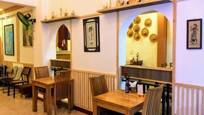 Ein Restaurantinneres mit Holztischen und -stühlen, einem an der Wand befestigten Regal mit Dekorationen und einem Spiegel, der den Innenraum reflektiert.
