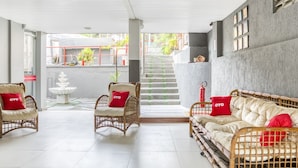 A spacious room with a white tiled floor, wicker furniture, and red cushions. - OYO Praia Hotel Recanto do Tomé - Salvador (Salvador)
