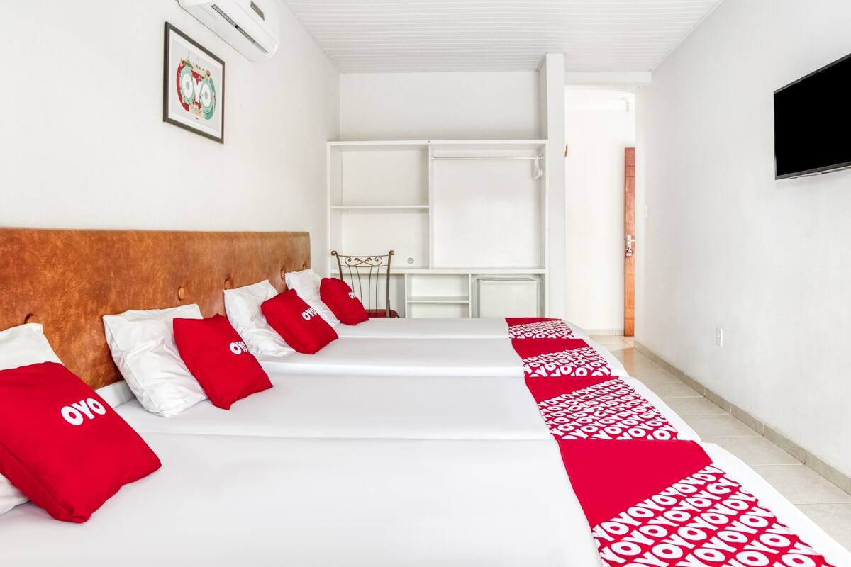 A hotel room with a bed, pillows, a TV, and a desk.