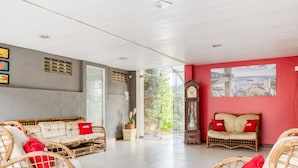 A spacious room with wicker furniture, a large window, and a red wall with a cityscape painting. - OYO Praia Hotel Recanto do Tomé - Salvador (Salvador)