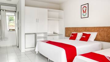 Una camera d'albergo con due letti, biancheria bianca, una coperta rossa e bianca, un armadio e un quadro appeso al muro.