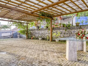 Un espacio exterior techado con pared de piedra, plantas en macetas y una mesa de mármol.