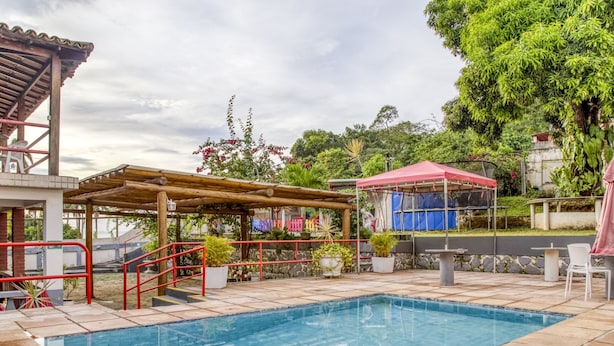 A swimming pool with a wooden deck, surrounded by potted plants and a covered seating area. - OYO Praia Hotel Recanto do Tomé - Salvador (Salvador)