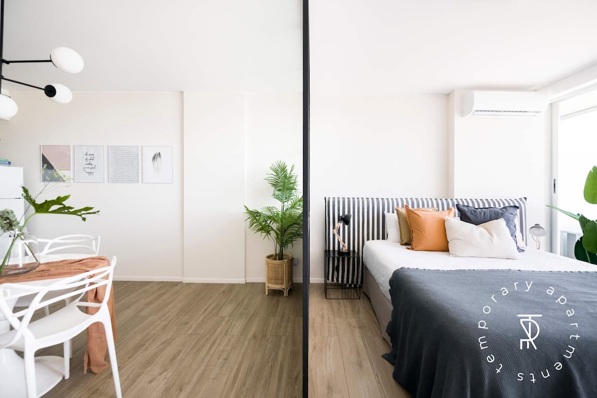A modern room with a bed, bedside table, lamp, and a potted plant.