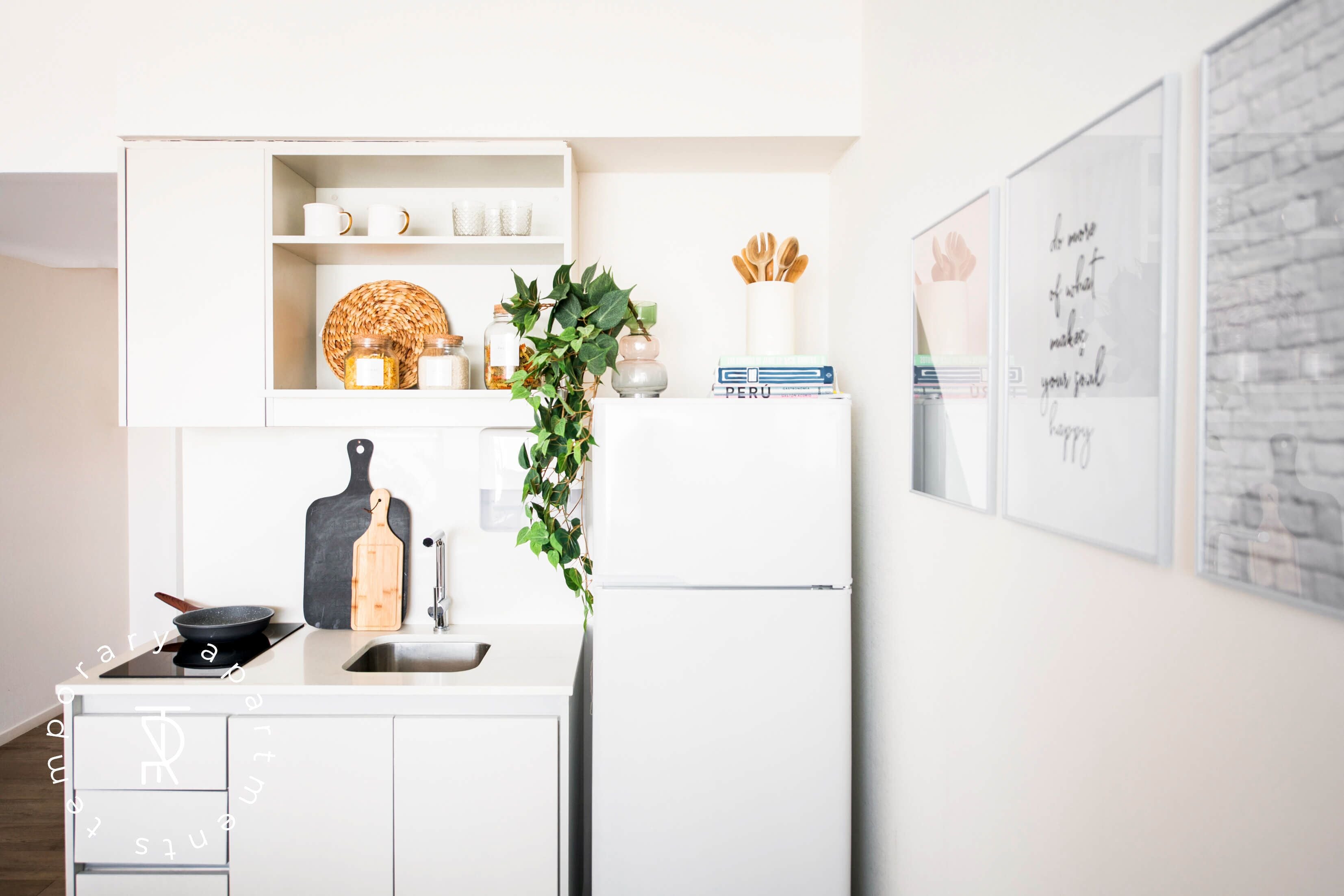 Een moderne keuken met witte kasten, een zwart snijplank, een koekenpan, een plant en een koelkast.