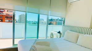 Habitación de hotel con una cama grande, vistas de la ciudad a través de ventanales y un balcón con vistas al agua.