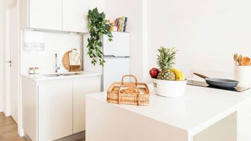 A modern kitchen with white cabinetry, a wooden floor, a hanging plant, a fruit bowl, and a wicker basket.
