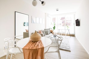 Una sala de estar moderna con un sofá blanco, una mesa de comedor con sillas y un ventanal con vistas a edificios.