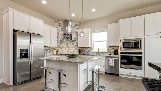 A modern kitchen with white cabinets, a stainless steel refrigerator, a marble backsplash, and a central island with bar stools. - Stay at Jake's Kalahari! Brand new house! (Round Rock)