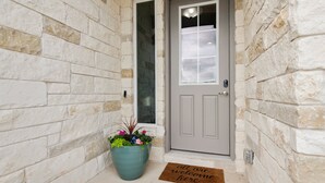 A stone wall entrance with a grey door, a large potted plant, and a welcome mat. - Stay at Jake's Kalahari! Brand new house! (Round Rock)