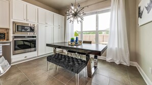 A modern kitchen with white cabinets, stainless steel appliances, a black bench, and a dining table with a chandelier. - Stay at Jake's Kalahari! Brand new house! (Round Rock)