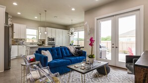 A modern kitchen with white cabinets, a blue sofa, and a dining area with clear chairs. - Stay at Jake's Kalahari! Brand new house! (Round Rock)