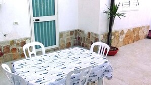 A patio area with a table set for four, surrounded by white plastic chairs, a potted plant, and a door with a glass panel. - Apartment nr. 2 in Villa Daniel, surrounded by greenery in VIESTE Gargano in P. (Vieste)