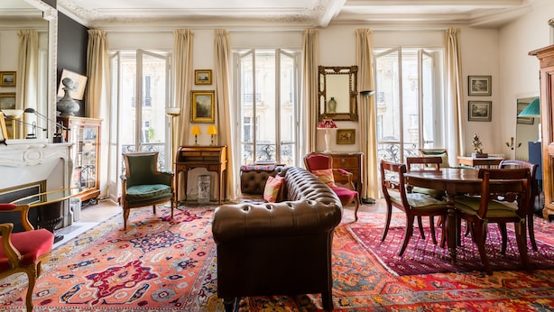 A spacious room with a large window, a fireplace, a sofa, a dining table with chairs, and a patterned rug. - Moments From Monet, by Veeve (Paris)