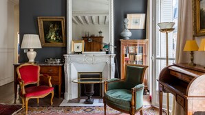 A room with a fireplace, a red chair, a green chair, a wooden desk, and a bookshelf. - Moments From Monet, by Veeve (Paris)