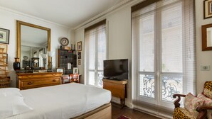 A bedroom with a large bed, a dresser, a television, and a window with blinds. - Moments From Monet, by Veeve (Paris)