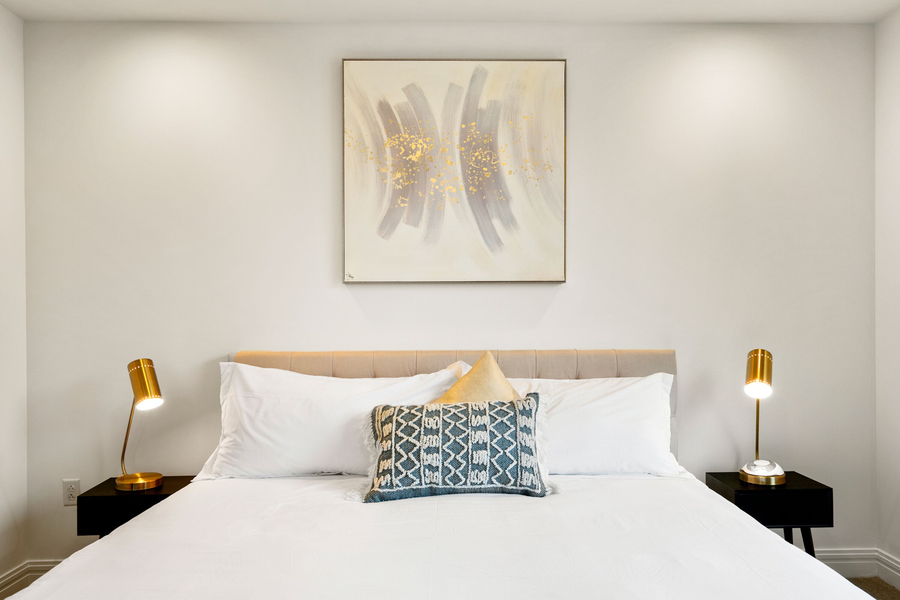 A neatly made bed with white linens, a patterned throw pillow, and two bedside lamps on black nightstands.