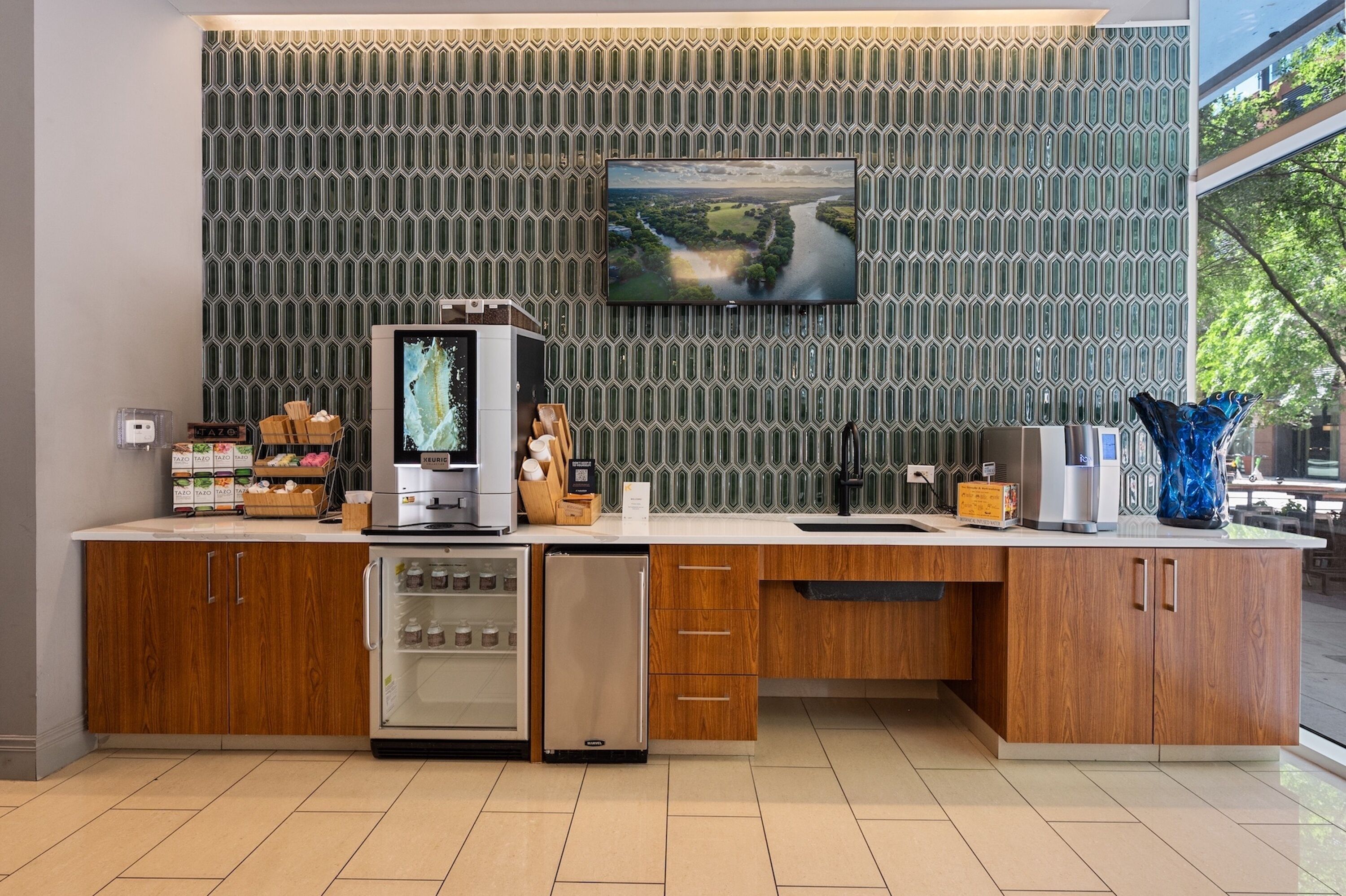 A modern kitchen with a built-in dishwasher, wooden cabinets, and a large flat-screen TV mounted on a patterned wall.